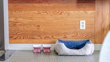 Een kamer met een wand van houten panelen, een wit stopcontact, twee roze en witte voerbakken voor huisdieren, en een blauw-wit huisdierenbed.