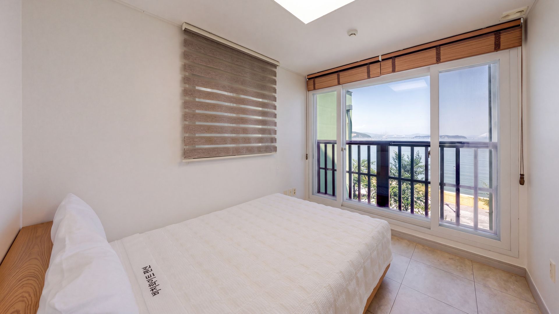 Un dormitorio con cama, ventana con persianas y vista al exterior.