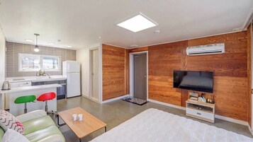 Habitación de hotel pequeña con kitchenette, una cama, televisor y un revestimiento de madera.