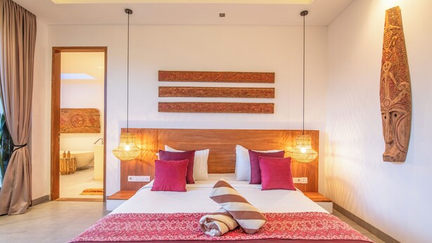A hotel room with a large bed, two bedside lamps, a wooden headboard, and a view of the bathroom. - Luxury 4BR Haven, Steps to Canggu's Beach Elegance (Canggu)