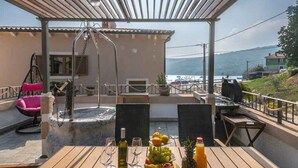 An outdoor dining area with wooden tables, a hanging chair, and a view of the sea. - Villa with sea views and private jacuzzi (Krnica)