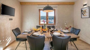 A dining area with a wooden table set for four, surrounded by black chairs. A large window with a view of boats and hills is visible behind the table. - Villa with sea views and private jacuzzi (Krnica)