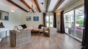 A spacious living room with wooden beams, a sofa, two wicker chairs, a coffee table, and large windows with curtains. - Villa mit Klimaanlage und Pool (Krnica)
