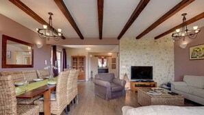 A spacious living room with a wooden dining table, wicker chairs, a grey sofa, and a television. - Villa mit Klimaanlage und Pool (Krnica)