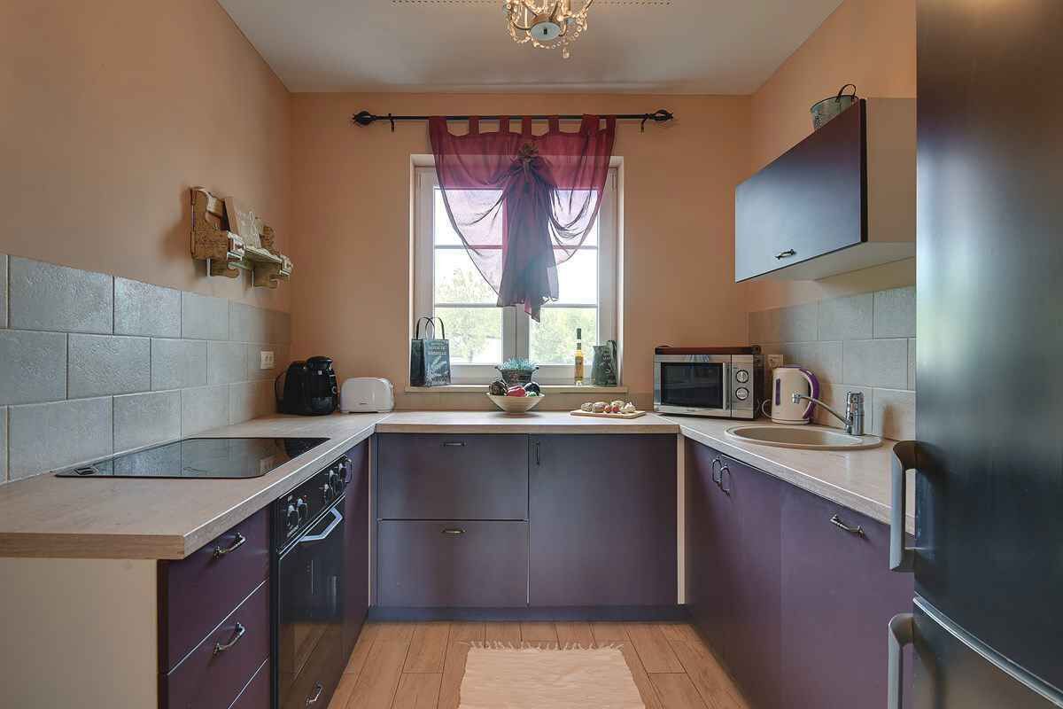 A compact kitchen with a built-in oven, a microwave, a sink, and a window with a curtain.