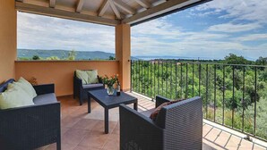 A covered balcony with wicker furniture, a table with a vase of flowers, and a view of greenery and distant hills. - Villa mit Klimaanlage und Pool (Krnica)