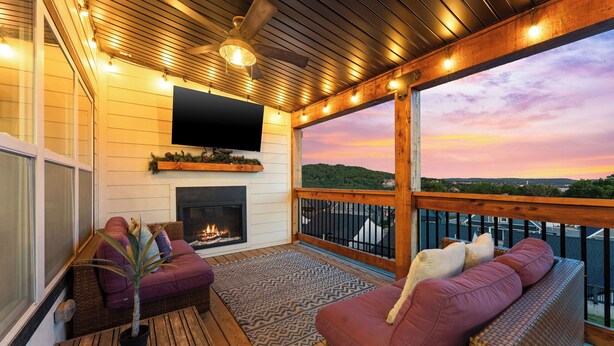 A cozy outdoor deck with a fireplace, comfortable seating, and a TV mounted on the wall.