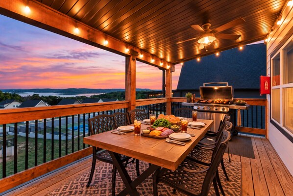 An outdoor deck with a wooden table set for dining, a grill, and a view of the landscape.