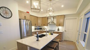 Una cocina moderna con una isla central, armarios de madera, electrodomésticos de acero inoxidable y un reloj grande en la pared.