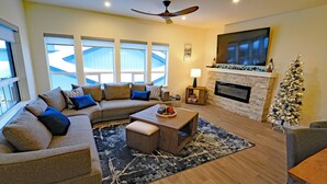 Una sala de estar moderna con un sofá modular, una chimenea, un televisor y un árbol de Navidad.