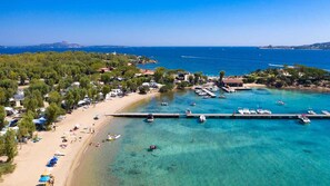 An aerial view of a coastal area with a sandy beach, clear blue waters, and several boats docked at a pier.