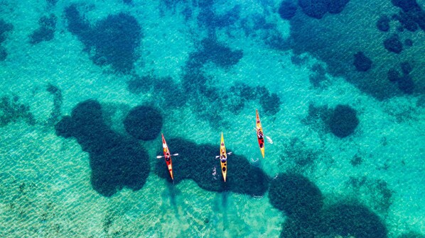 An aerial view of a clear blue sea with three kayaks.