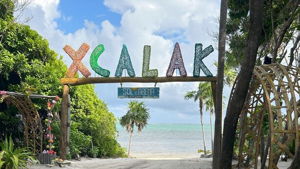 Una entrada a la playa con un letrero que dice "XCALAK" y "SOL ARENA".