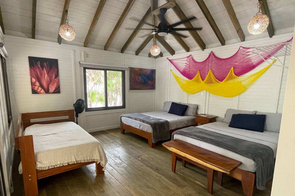Ein Zimmer mit drei Holzbetten, einem Deckenventilator und einem Fenster mit Blick auf Grünflächen.