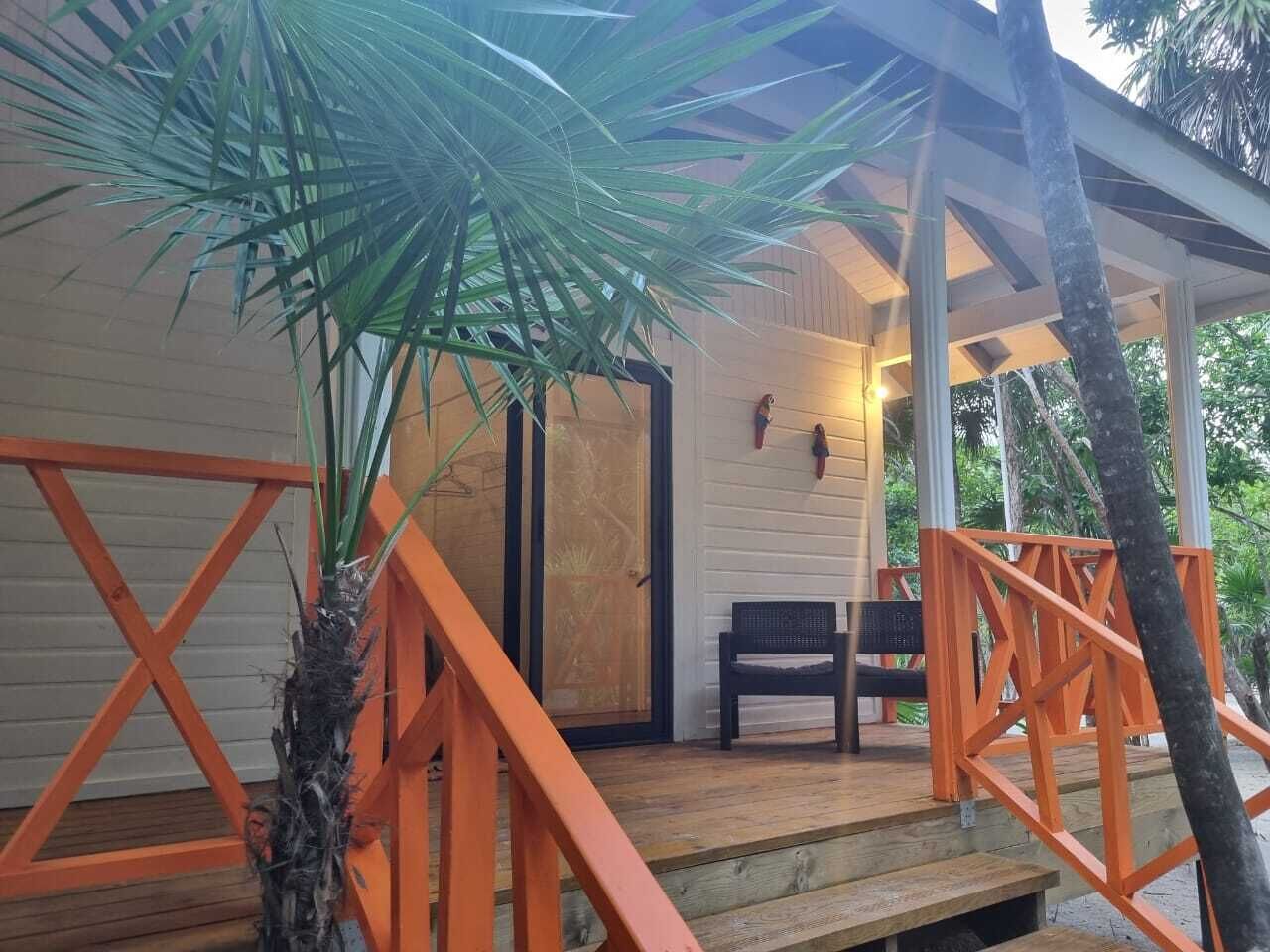 Une terrasse en bois avec des rampes orange, un banc et une porte donnant sur un espace abrité équipé d’un luminaire fixé au mur.