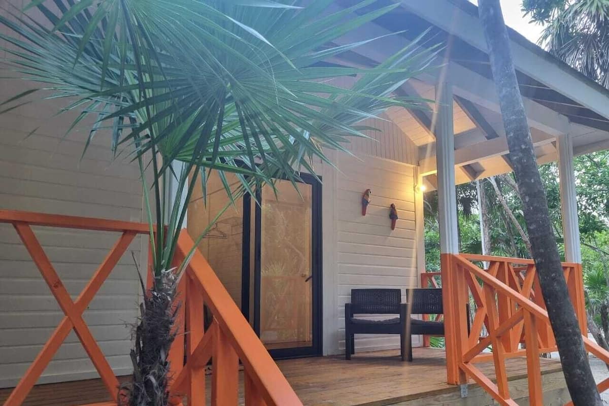 Une terrasse en bois avec des rampes orange, un banc et une porte donnant sur un espace abrité équipé d’un luminaire fixé au mur.