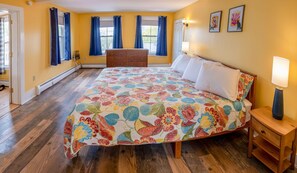 A bedroom with a floral bedspread, wooden floor, and a dresser. - Historic 2 Cats Inn-Free Breakfast-Georgia Room (Bar Harbor)