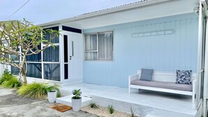A modern house with a light blue exterior, a covered porch with a bench, and potted plants. - Pipi Palace Ruakaka – Ideal for Work & Family Stays (Ruakaka)