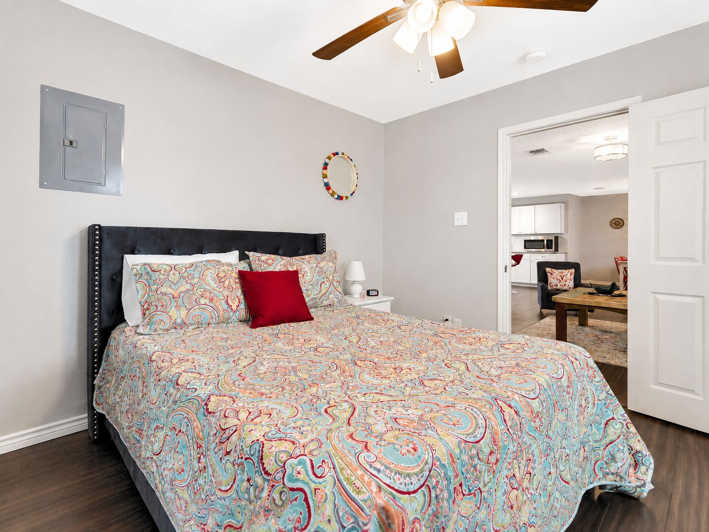 Une chambre à coucher comprenant un lit, une table de chevet, un ventilateur de plafond et donnant sur l’espace de vie adjacent.