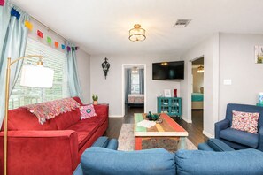 A living room with a red sofa, blue armchairs, a wooden coffee table, and a TV mounted on the wall. - Lone Star Fiesta with Game Room Near Alamodome Ultimate Retreat for Fun & Rel... (San Antonio)
