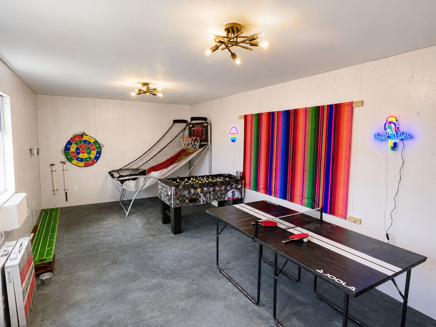 Une pièce avec une table de baby-foot, un jeu de fléchettes et un mur rayé aux couleurs vives.