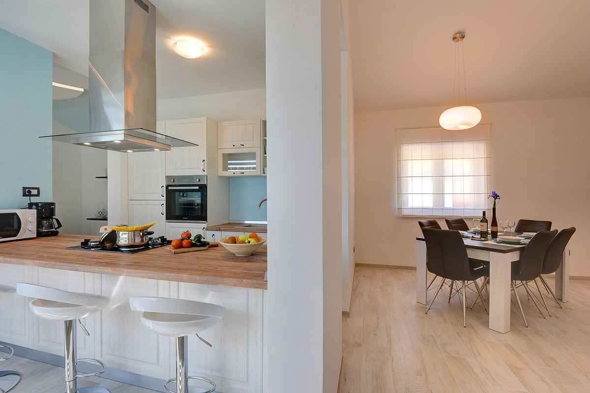 Una cocina moderna con armarios blancos, una isla central con taburetes y un comedor con mesa y sillas.