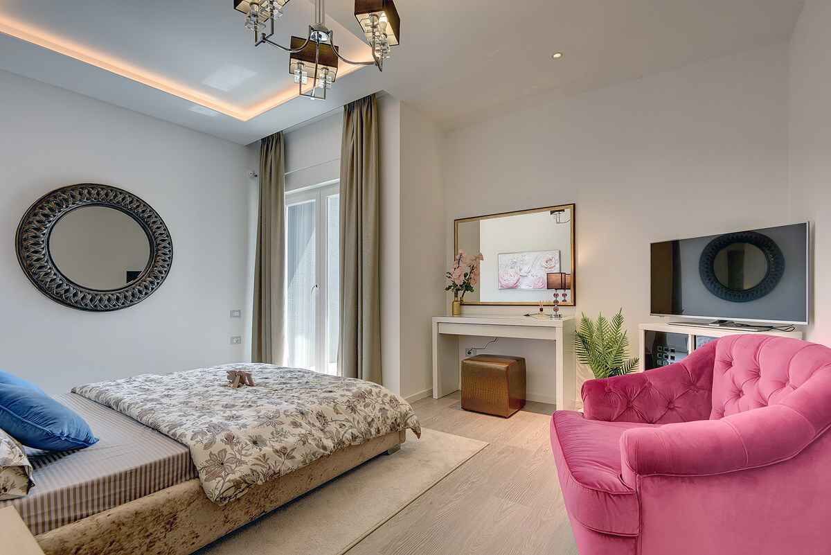 A modern bedroom with a bed, a pink chair, a TV, and a desk.