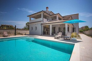 Une maison à deux étages dotée d’une piscine, d’un espace salon extérieur et d’un patio couvert.