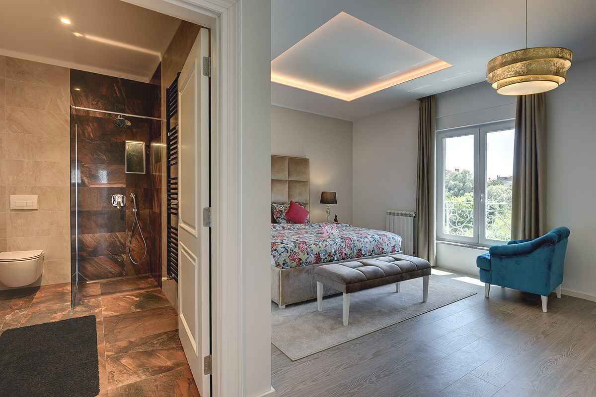 Un dormitorio moderno con una cama grande, un banco, una silla azul y vistas al exterior a través de una ventana.