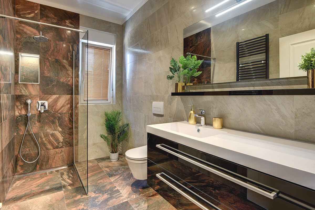 A modern bathroom with a glass-enclosed shower, a white sink, and a marble-tiled floor.