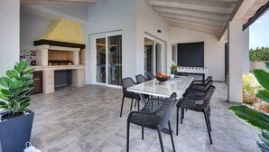An outdoor patio with a dining table, chairs, a grill, and a TV screen. - Villa with heated pool (Premantura)