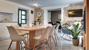 Une cuisine moderne avec un mur d’accent en pierre, un coin repas avec une table et des chaises en bois, et un grand téléviseur fixé au mur.