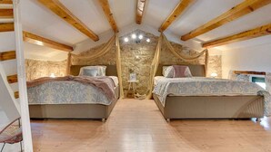 Une chambre avec deux lits, des poutres en bois, des murs en pierre et une petite table avec une lampe.