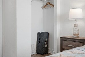 Una camera da letto con un letto, un comodino con una lampada, un appendiabiti in legno e una borsa nera con un logo.