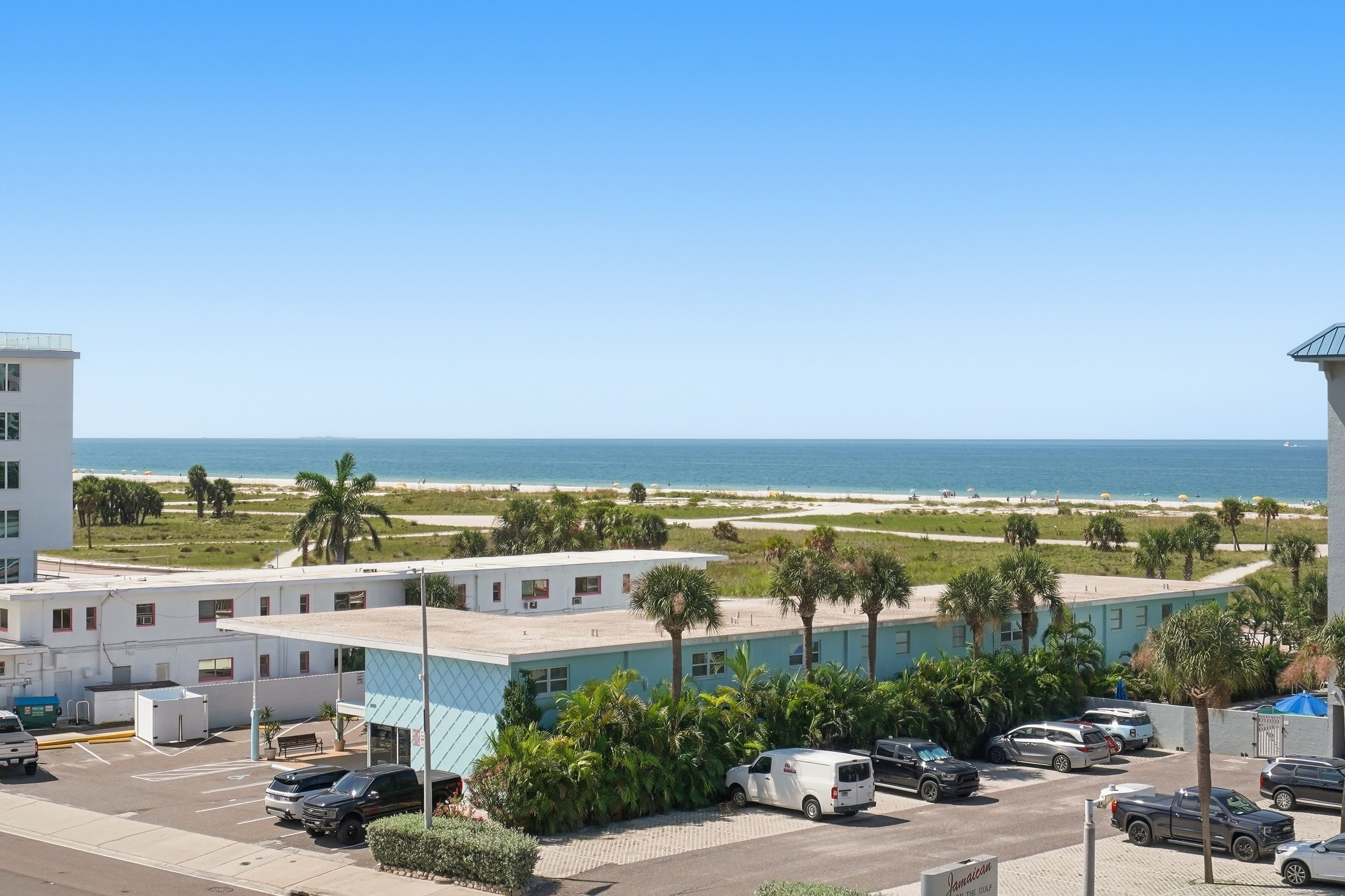 A coastal hotel with a parking lot, a view of the beach, and a clear sky.