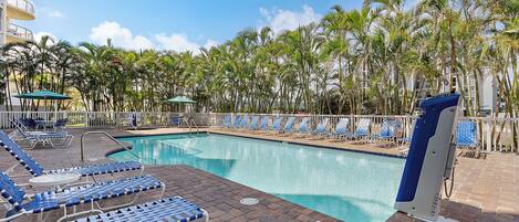 A pool area with lounge chairs and umbrellas, surrounded by palm trees.