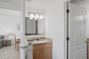 A bathroom with a sink, mirror, and vanity. There is a door leading to another room.