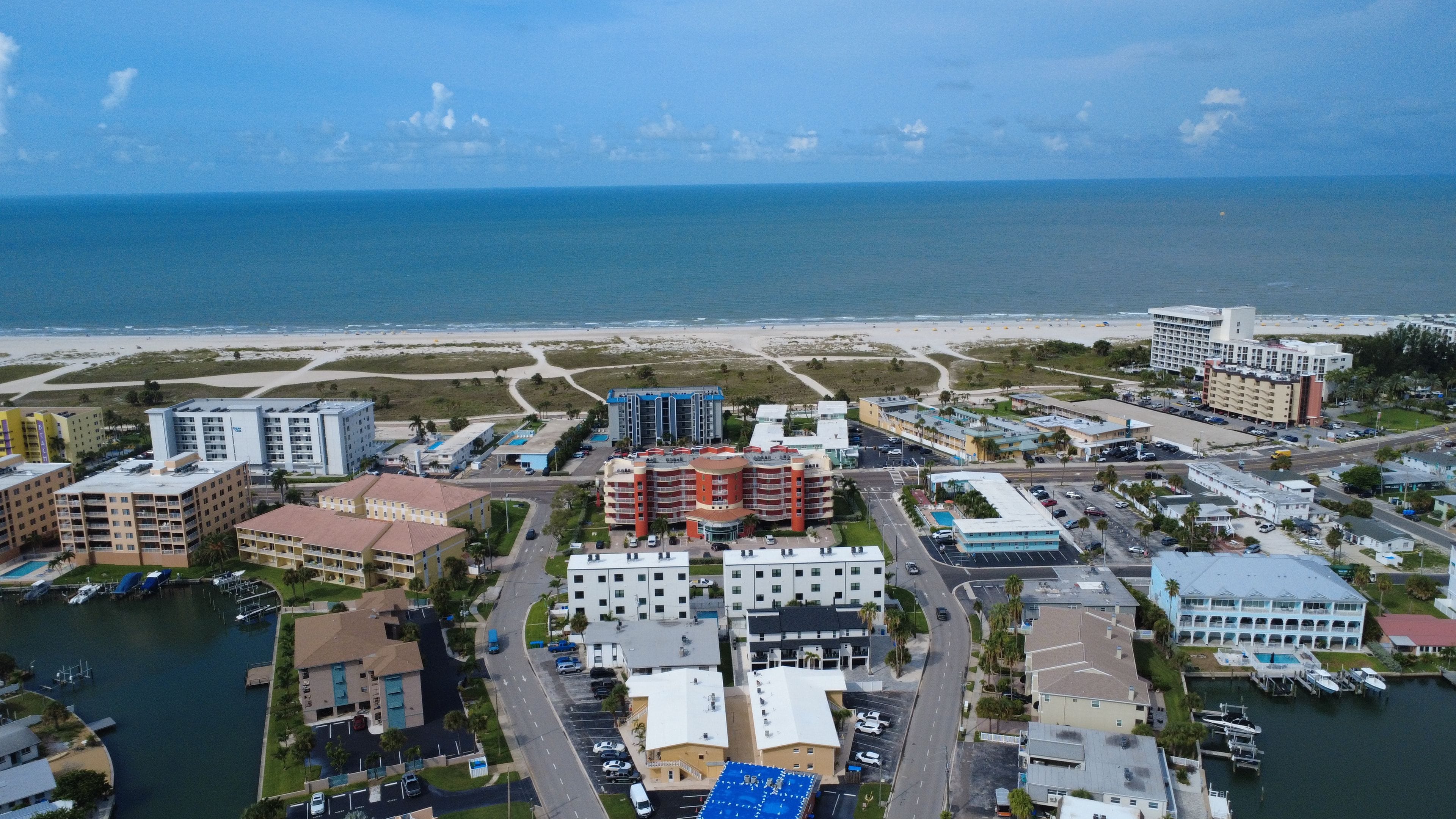 Vista aérea de una zona hotelera costera con varios edificios, un puerto deportivo y una playa al fondo.