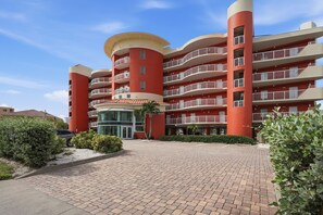 A multi-story hotel with a red facade, balconies, and a paved entrance area.