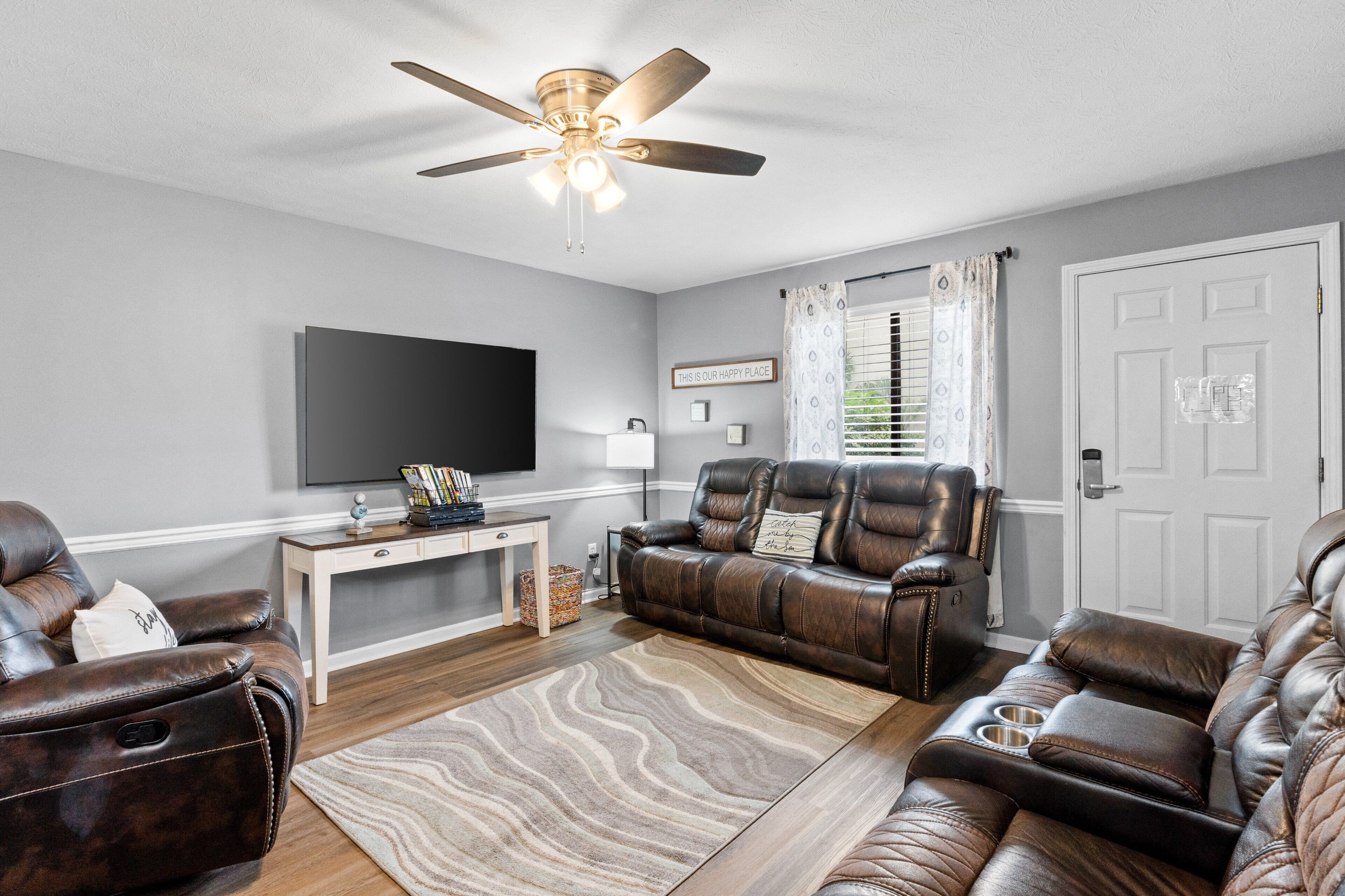 A living room with a ceiling fan, leather sofas, a flat-screen TV, and a wooden coffee table.