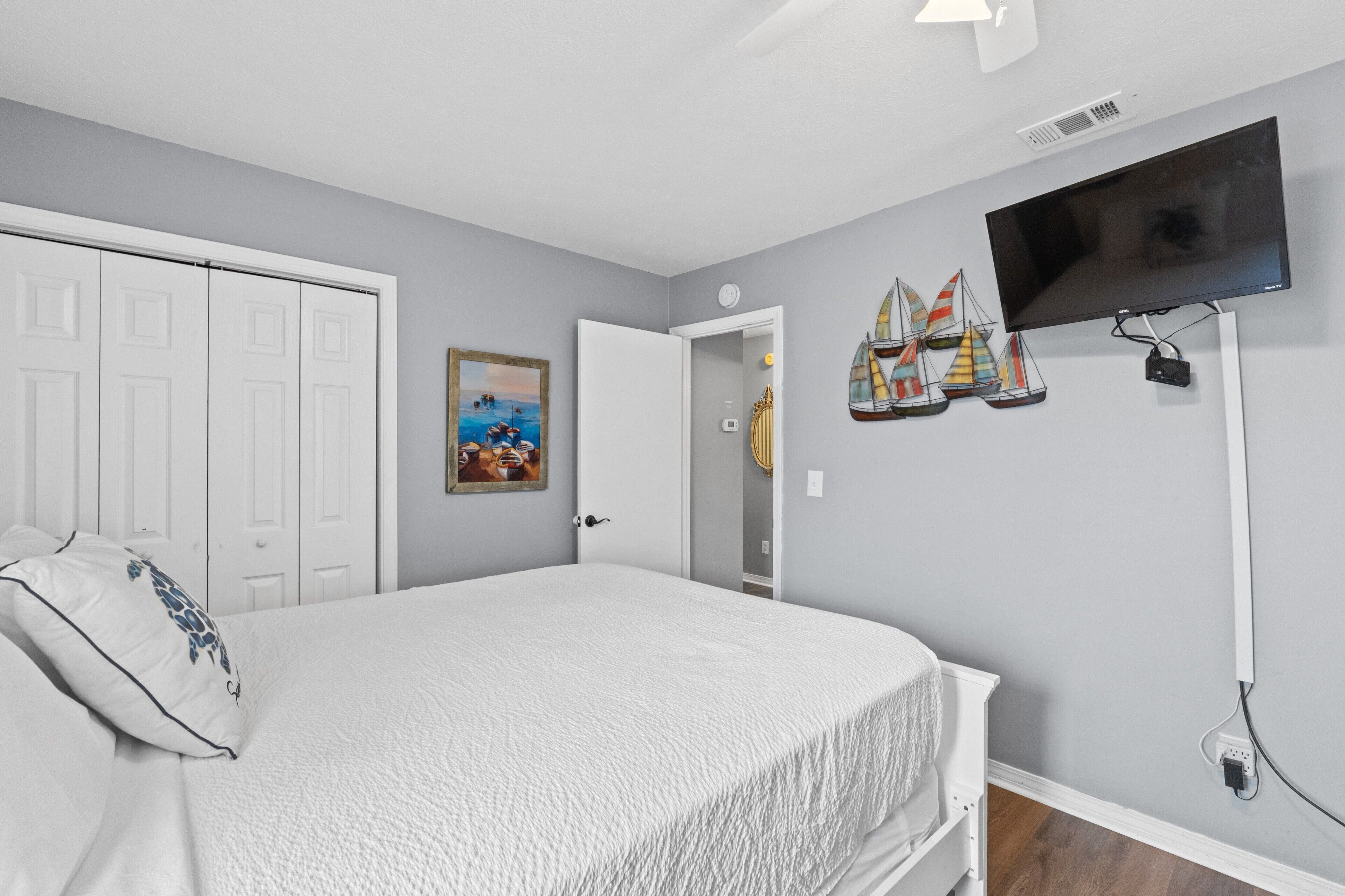 A bedroom with a bed, a TV mounted on the wall, and a door leading to another room.