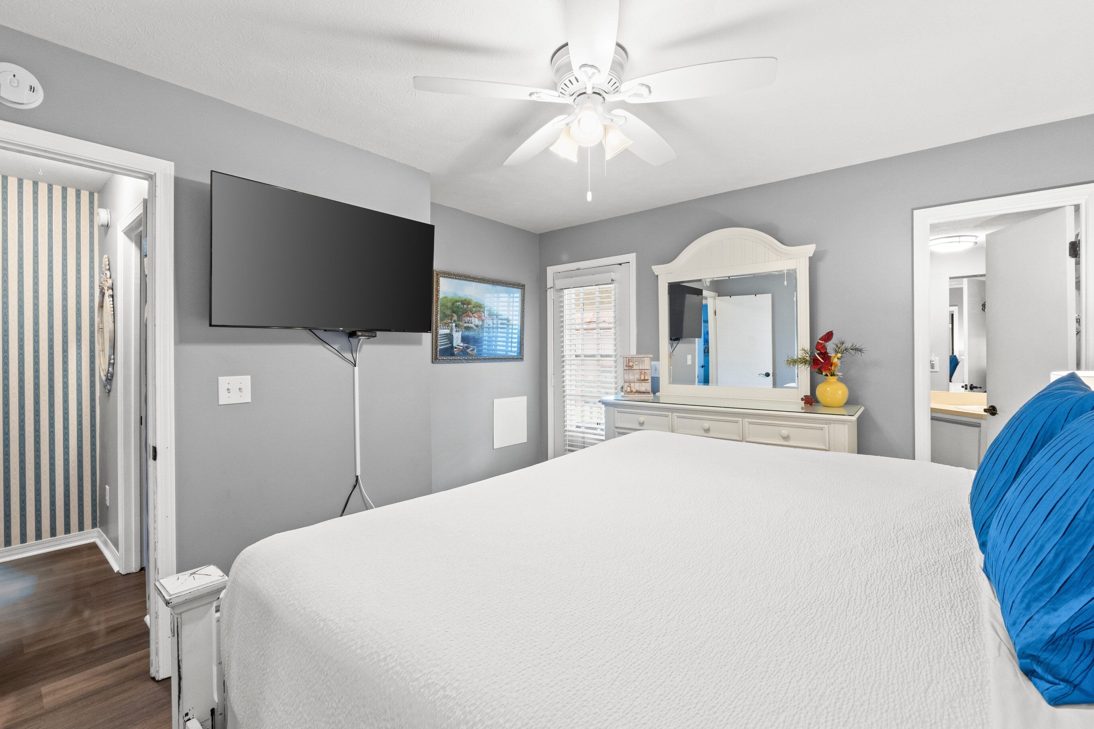 Une chambre à coucher comprenant un lit, un ventilateur de plafond, une télévision, une commode et un miroir.
