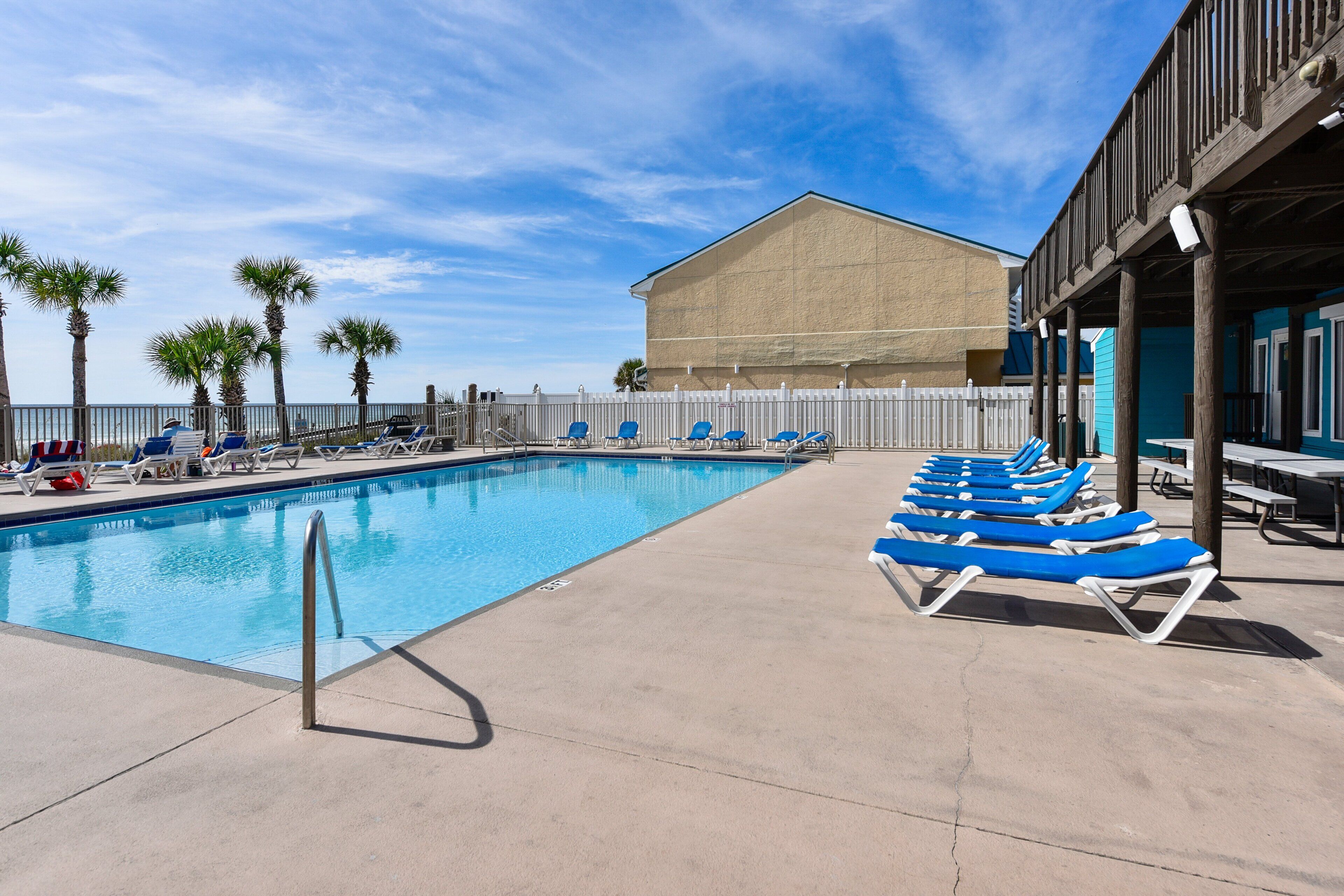 A swimming pool with blue lounge chairs and a white fence.