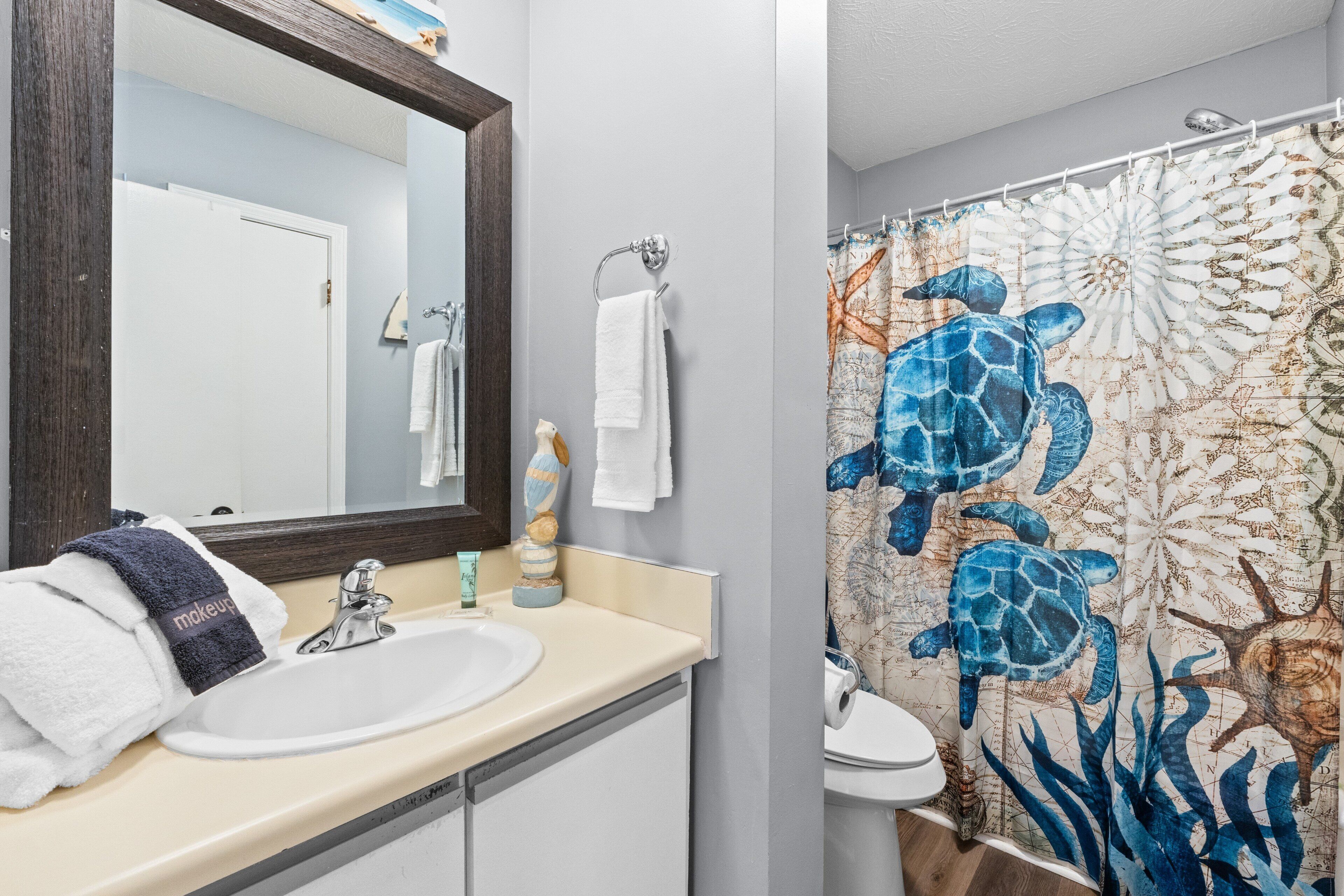 A bathroom with a sink, mirror, and a shower curtain with a sea turtle design.