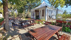 Un espace extérieur aménagé avec des tables et des bancs en bois, entouré d’arbres et abrité par un pavillon couvert.