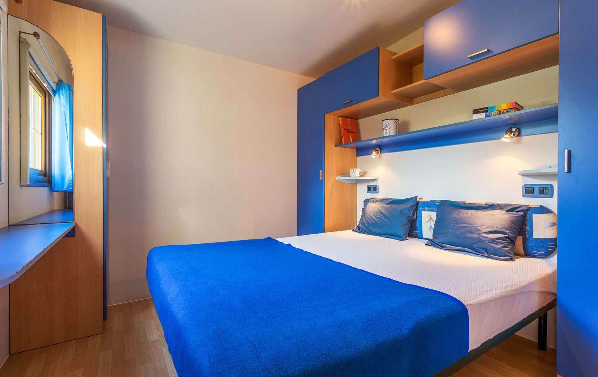 Ein Schlafzimmer mit einem Bett, einem Spiegel, einem Regal mit Gegenständen und einem Fenster.