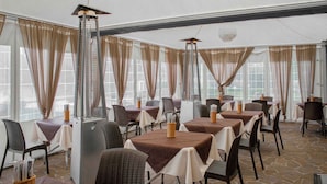 Un restaurant dont les tables sont recouvertes de nappes marron, avec des chaises en osier et un sol en pierre.