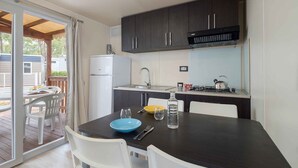 Une cuisine compacte avec des meubles de couleur sombre, un réfrigérateur blanc et un petit coin repas comprenant une table et des chaises.