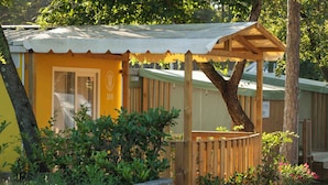 Un bâtiment jaune doté d’un porche en bois, entouré de verdure et d’arbres.