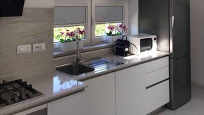A modern kitchen with a built-in gas stove, a stainless steel refrigerator, and a window with a view of greenery. - Holiday apartment with a/c (Duino-Aurisina)